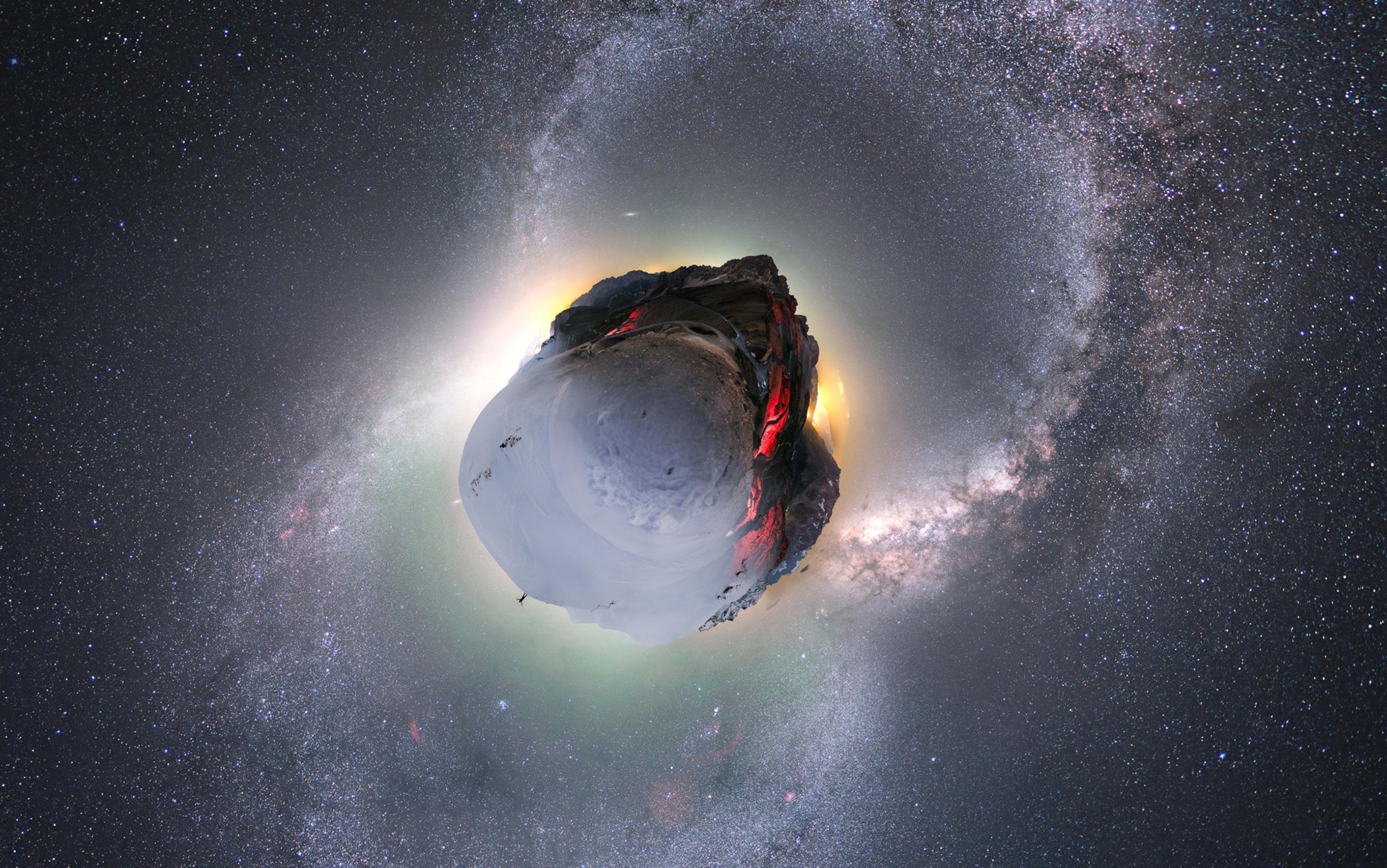 Tiny planet photo of a snowy mountain under a starry sky and Milky Way galaxy with glowing horizon.