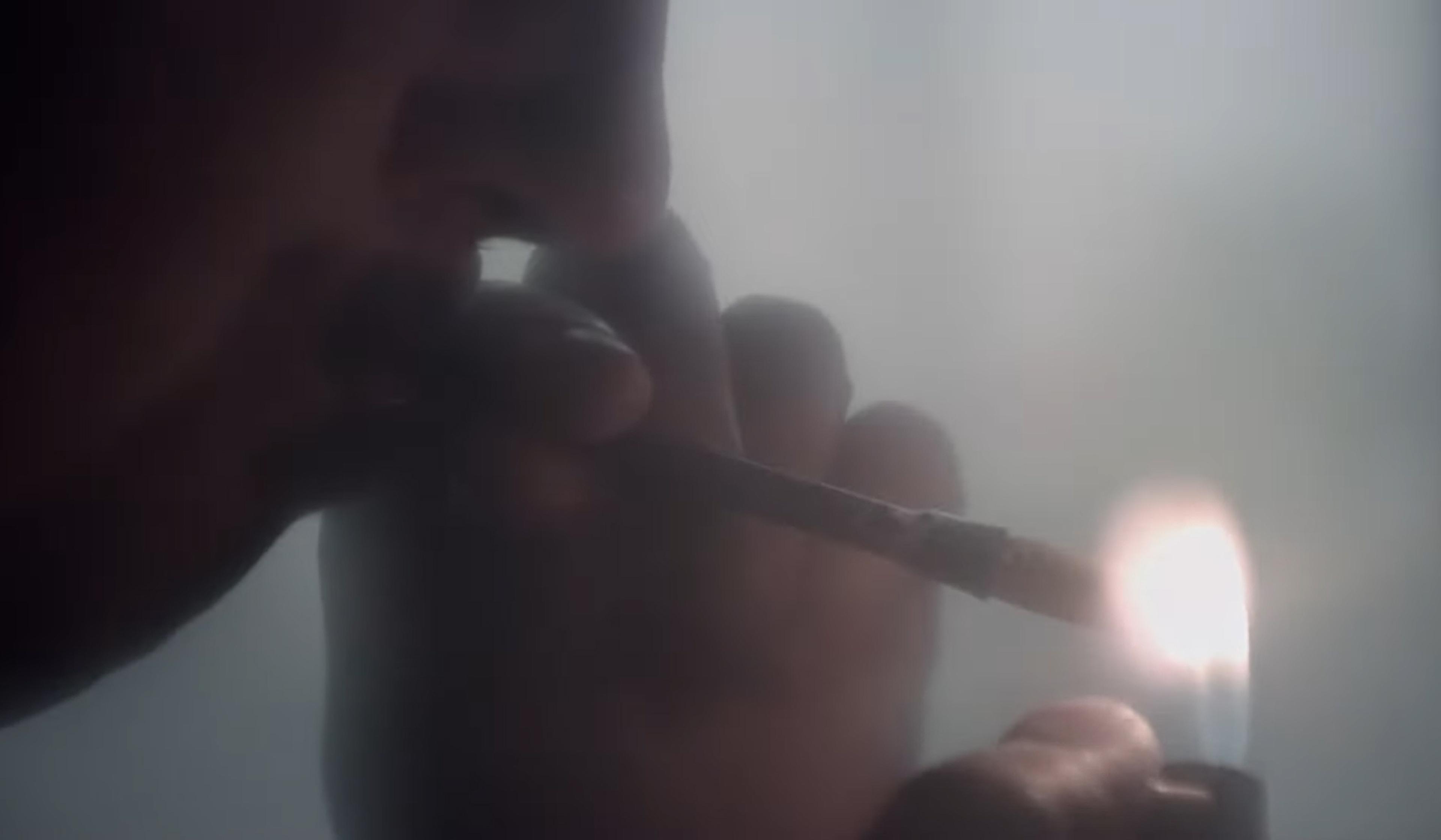 Close-up of a person lighting a cigarette with a lighter in a dim, smoky environment.