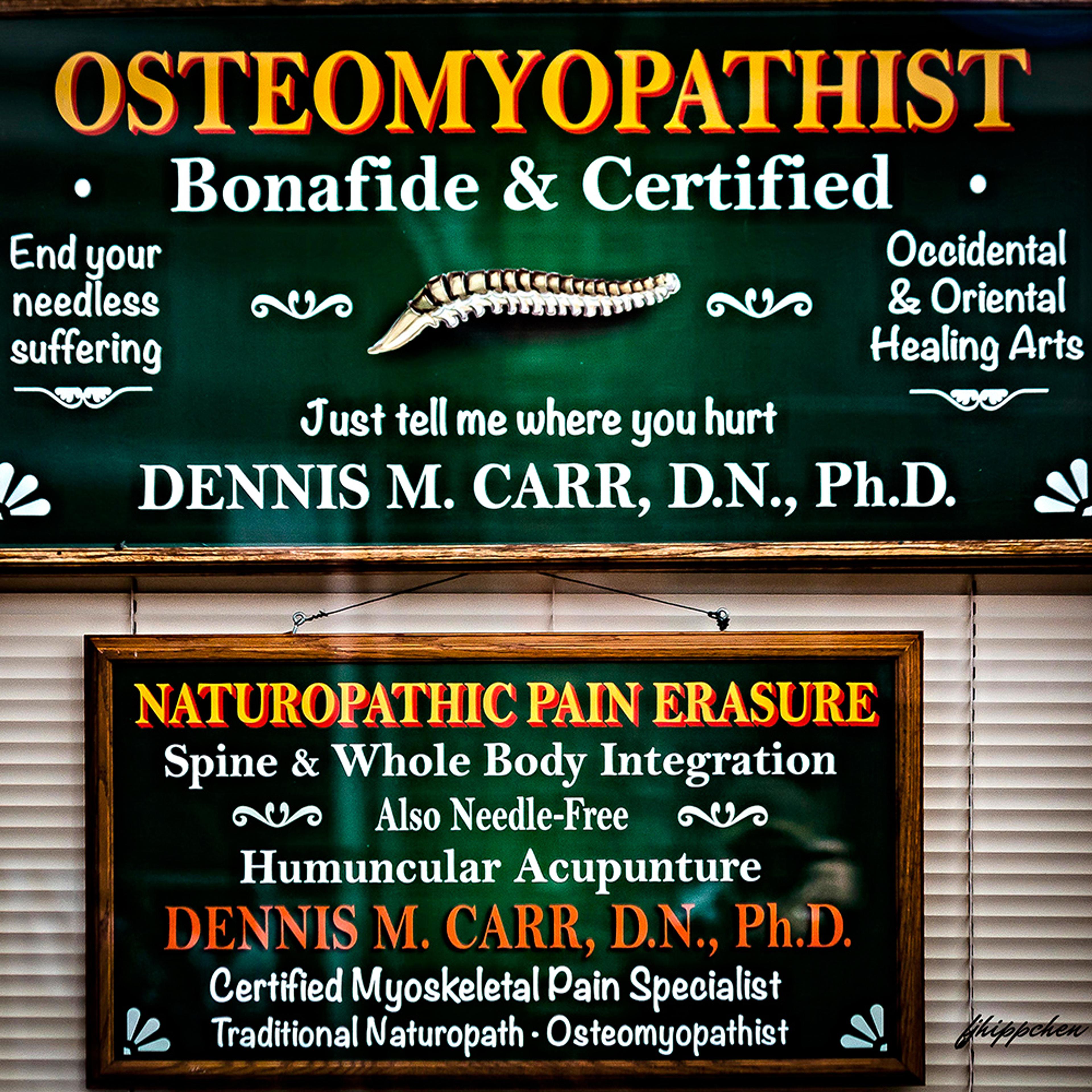 Photo of two signage boards for an osteomyopathist, advertising naturopathic pain erasure and various treatments by Dennis M. Carr.
