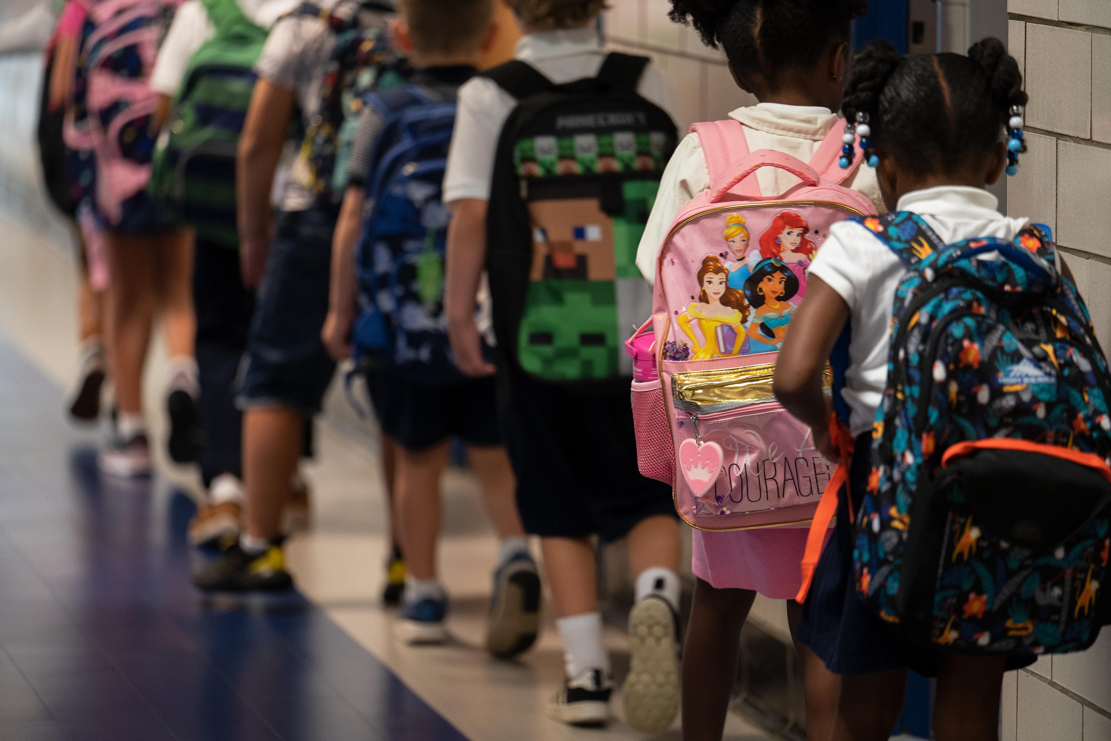 Photo of children with backpacks walking in a school corridor.