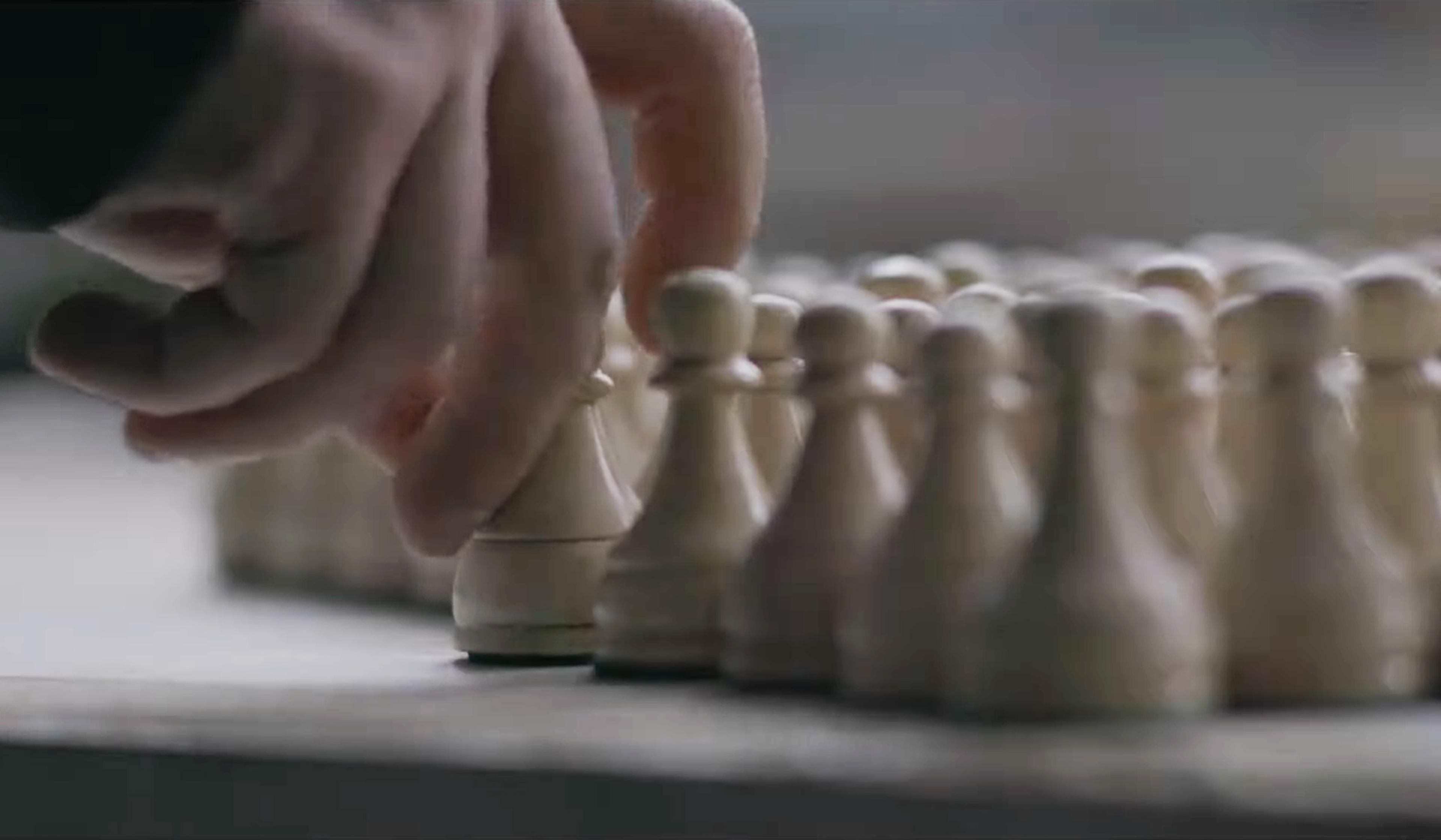 A hand placing a chess pawn among other pawns on a chessboard.