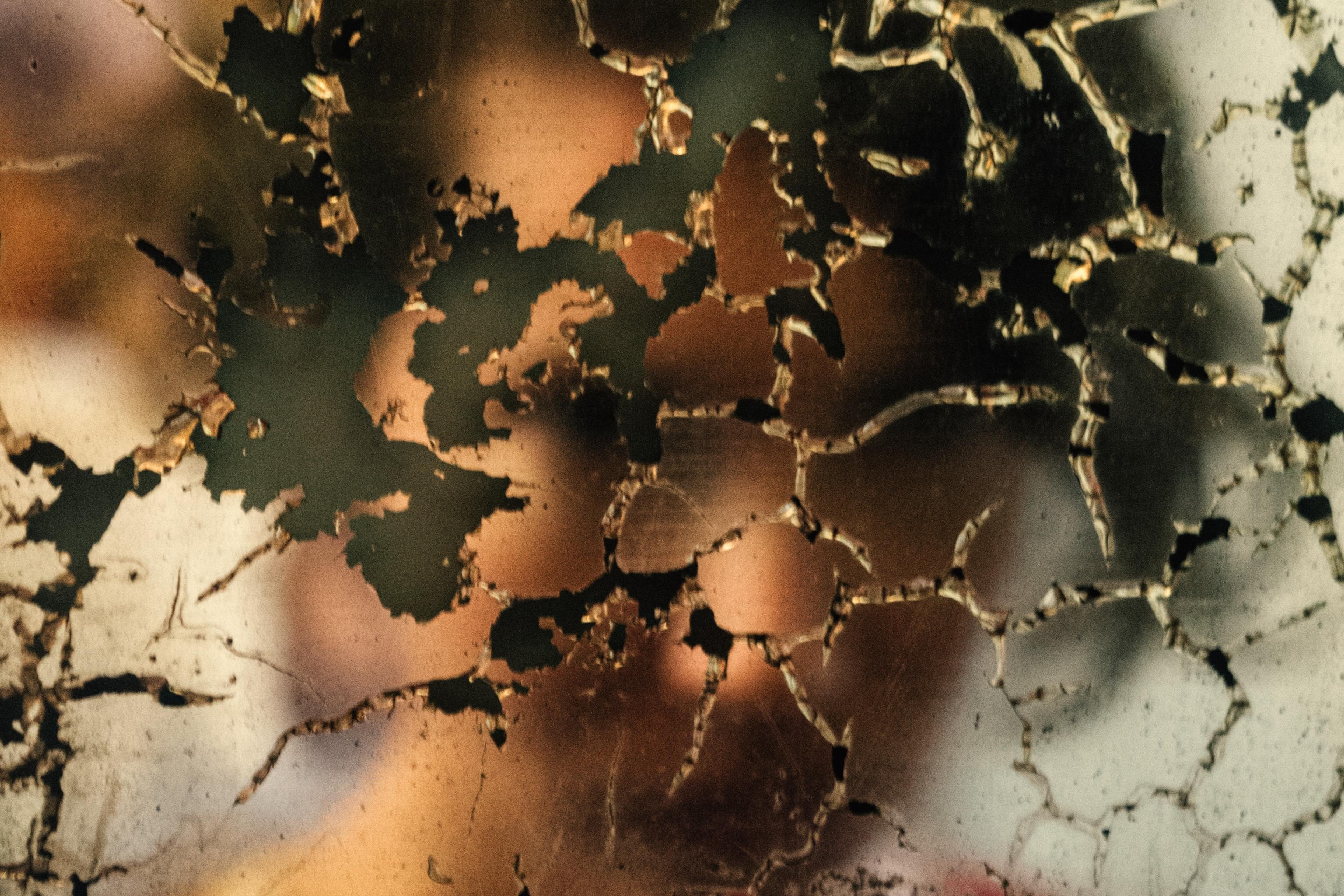 Photo of a blurred background visible through cracked peeling paint on a surface in earthy tones.