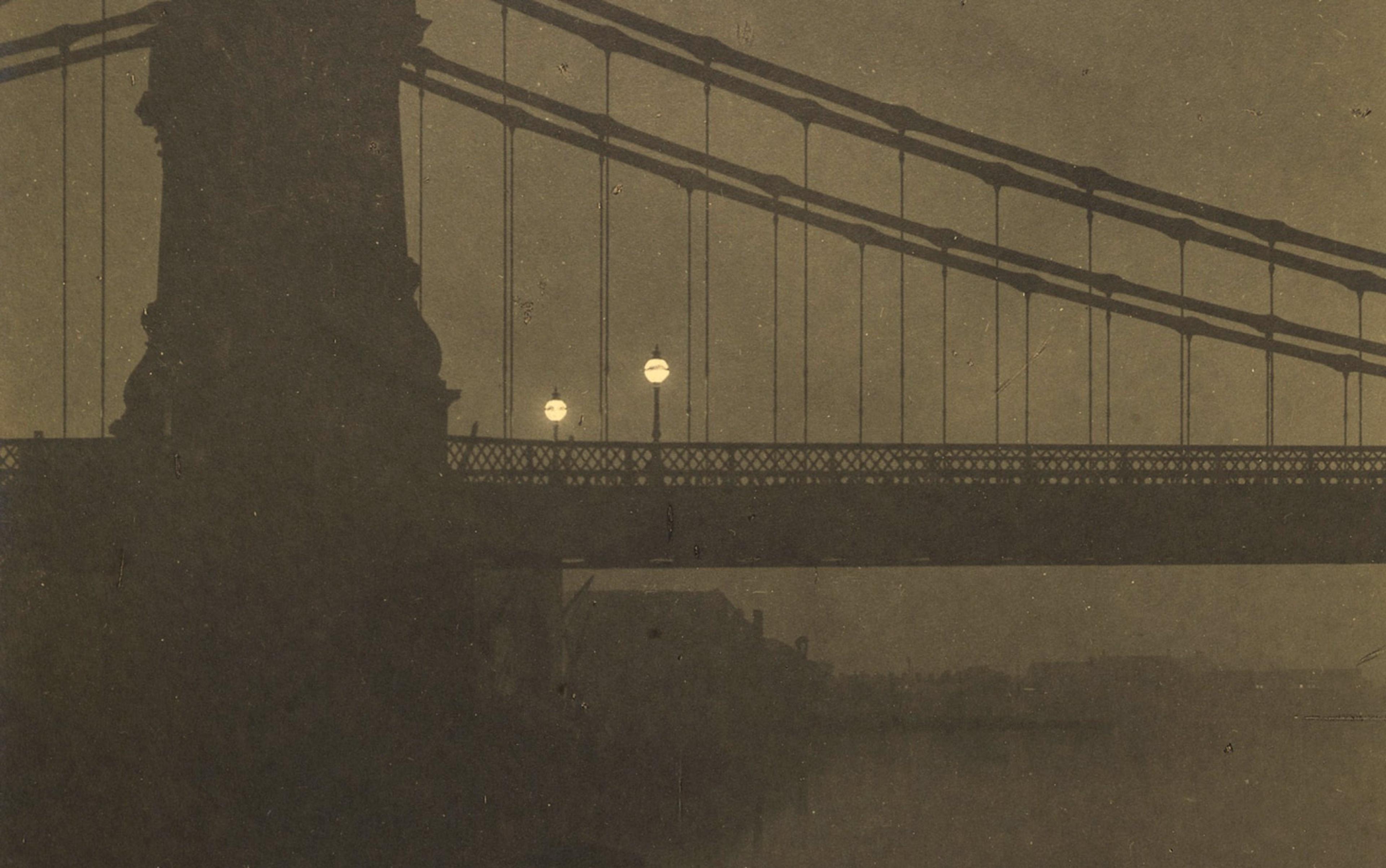 Sepia-toned photograph of a suspension bridge at night with streetlights illuminating the structure and subtle reflections on water.