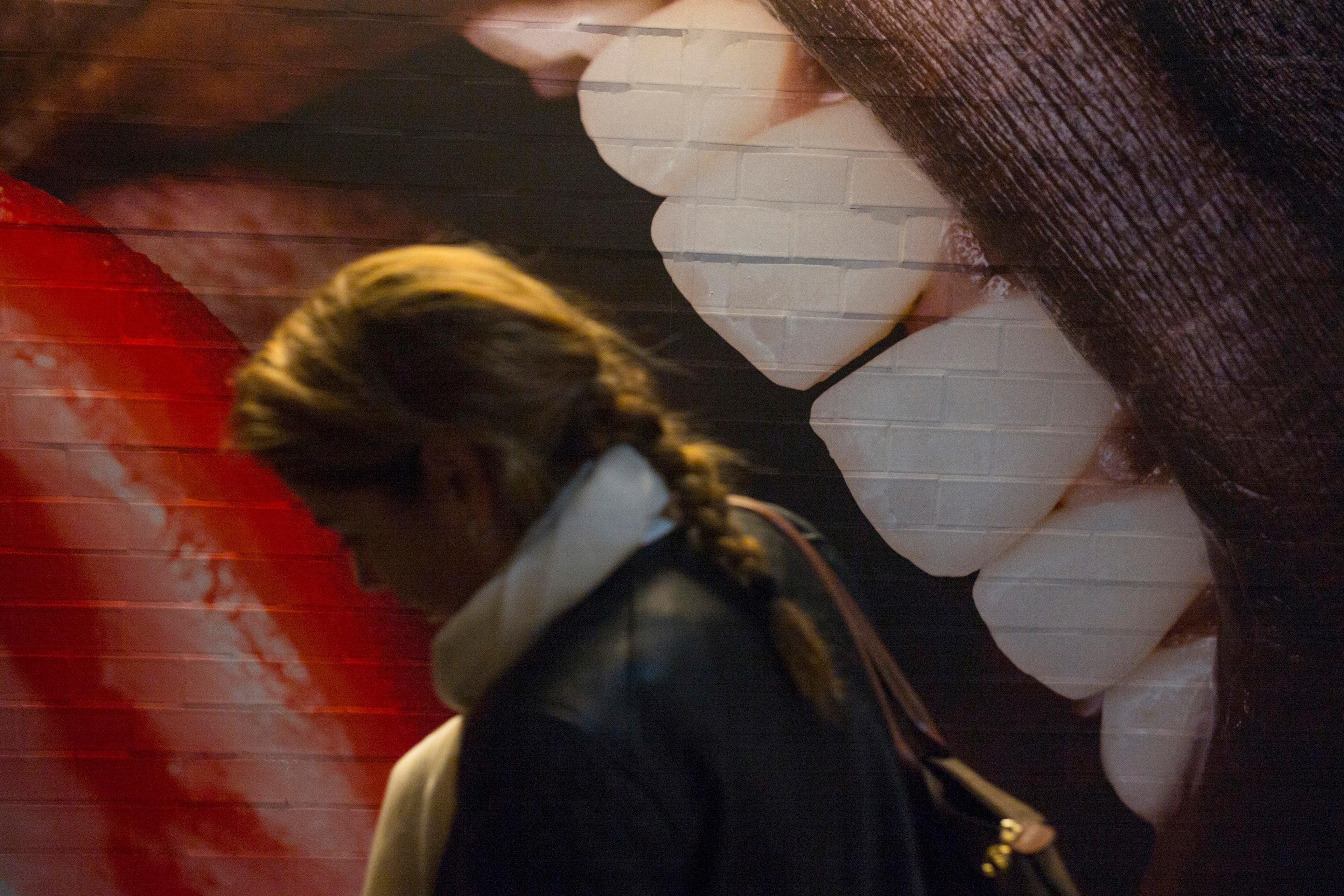 Photo of a person walking past a mural of large, realistic teeth and lips on a wall, with the mural dominating the background.
