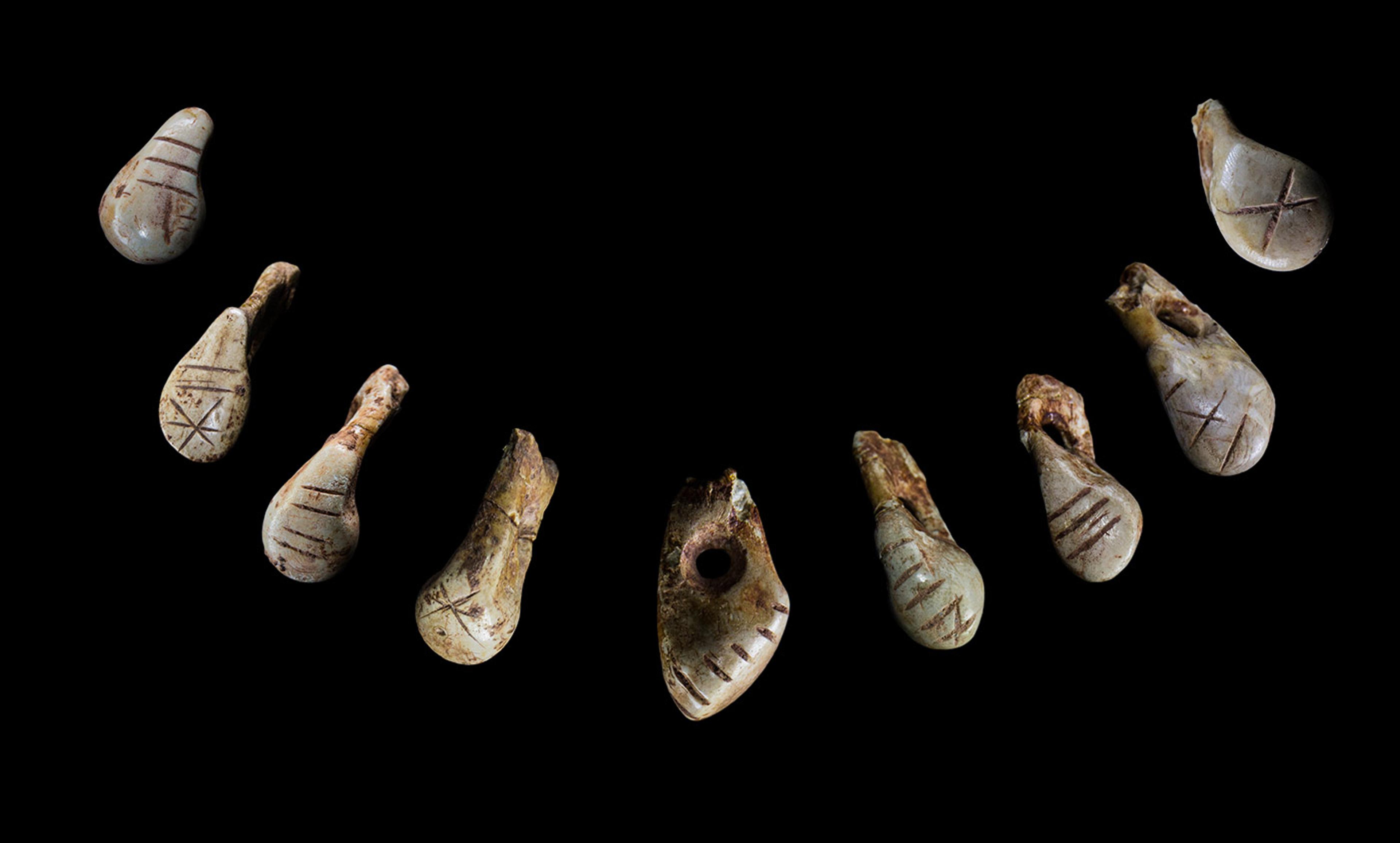 Ancient pendants arranged in a semicircle on a black background. The pendants feature engraved lines and various shapes.