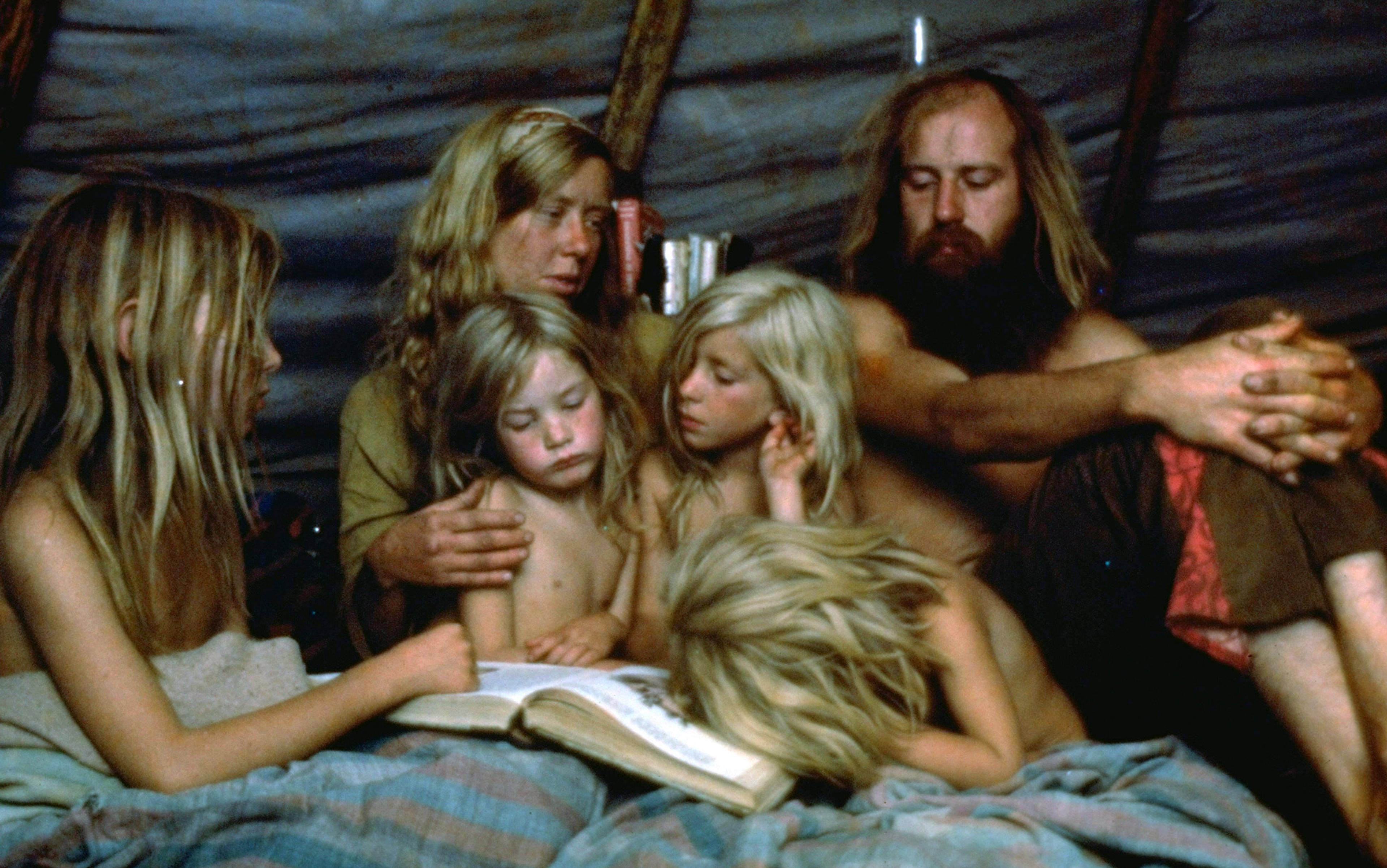 Photo of a family of six sitting together, reading a book in a dimly lit tent.