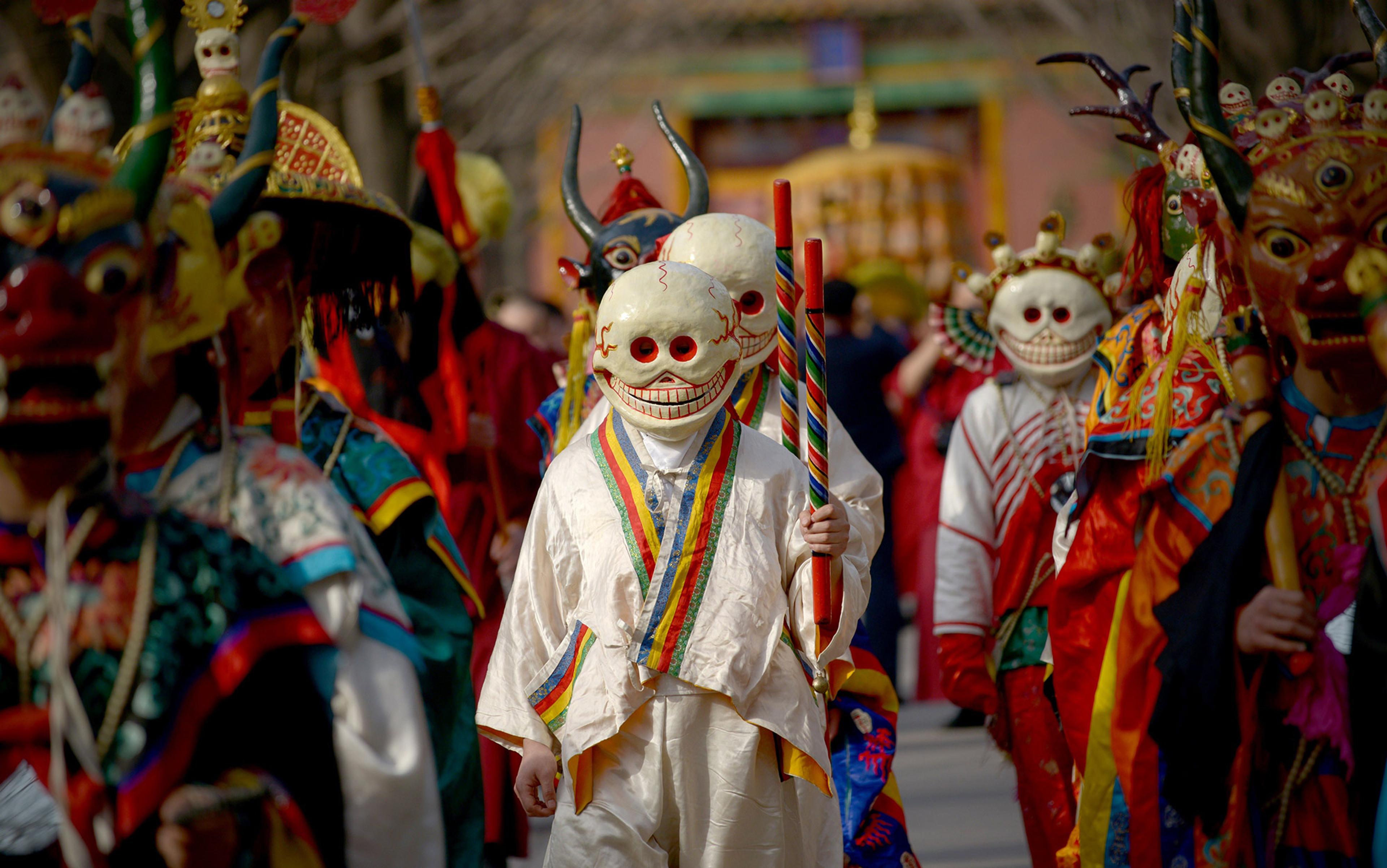 People in colourful traditional costumes and masks, holding staffs, participating in a cultural or religious procession.
