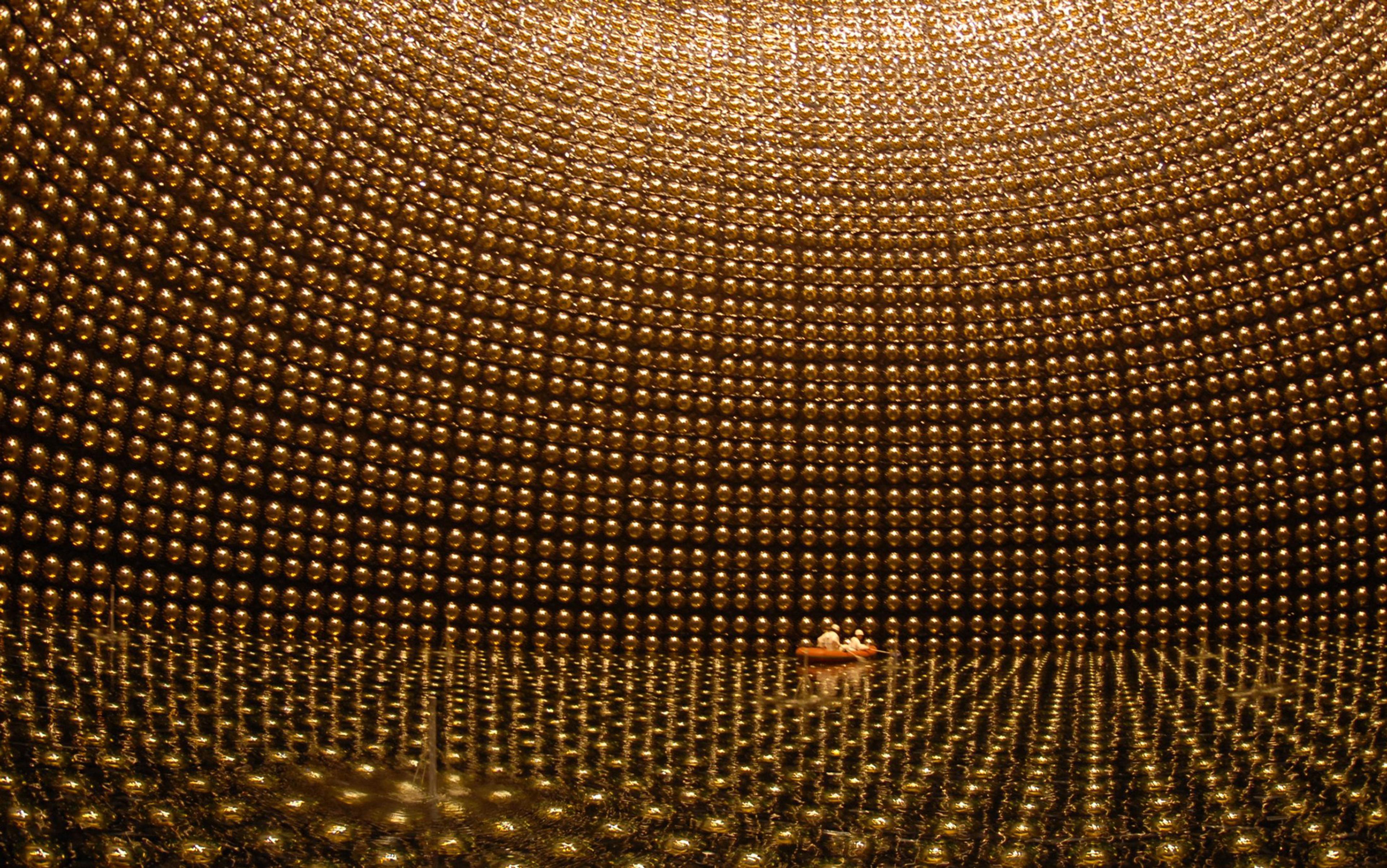 A large, spherical room with golden reflective panels on walls, ceiling and floor, featuring a boat with people near the centre.