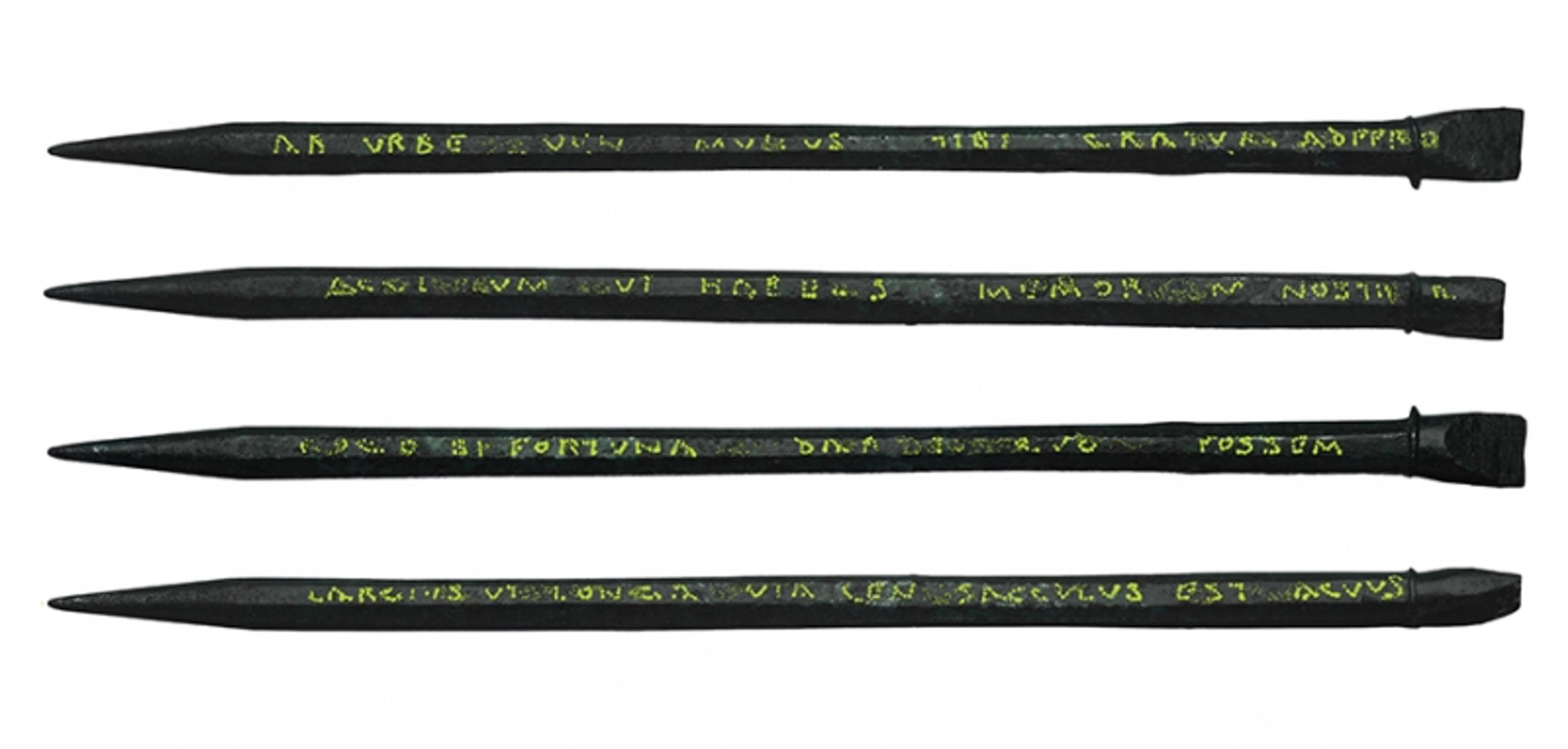 Four ancient writing styli with inscribed text, aligned horizontally and parallel to each other on a white background.